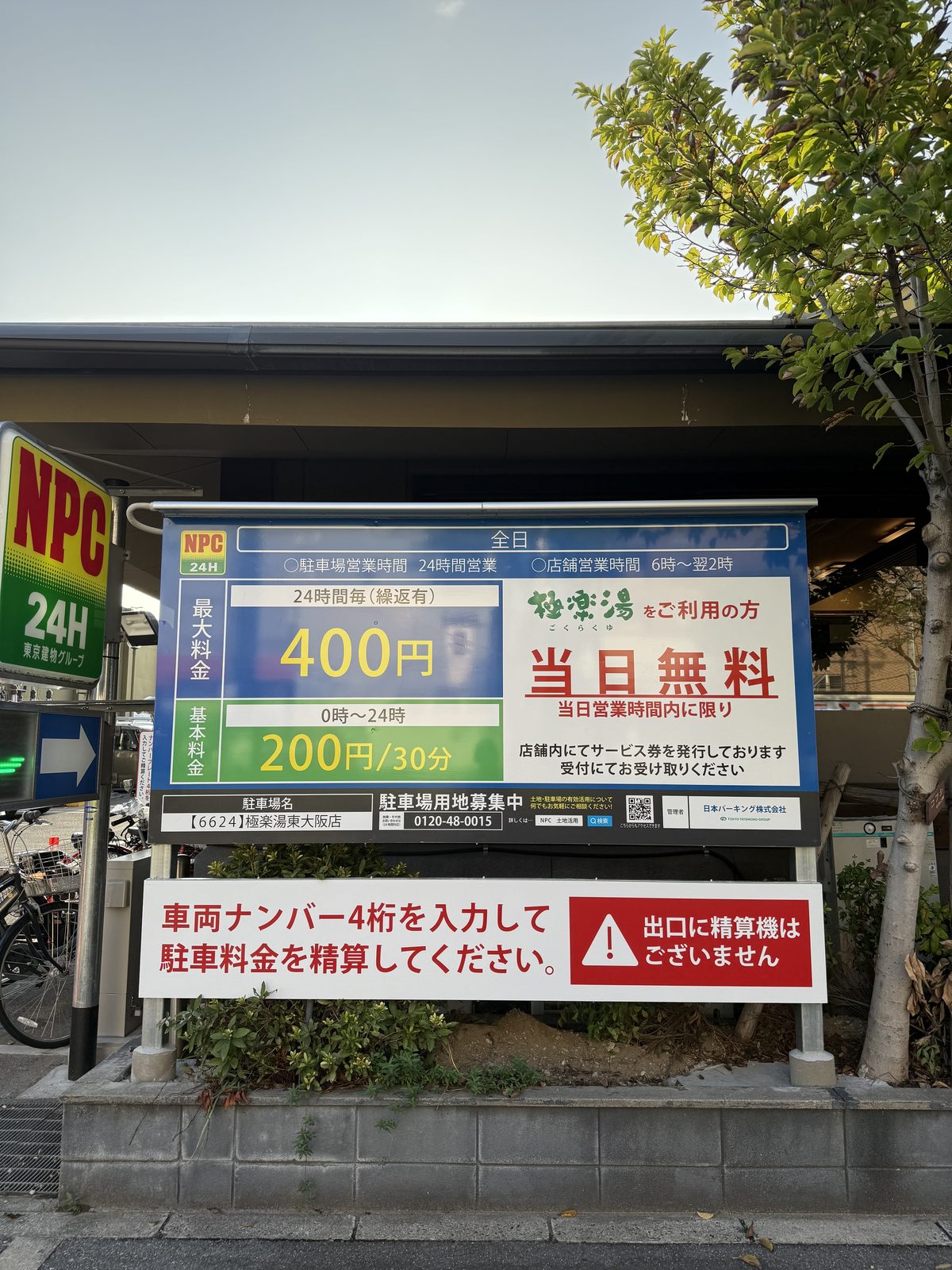 NPCコインパーキングの料金看板。最大料金24時間400円、極楽湯利用者は当日無料と書かれている