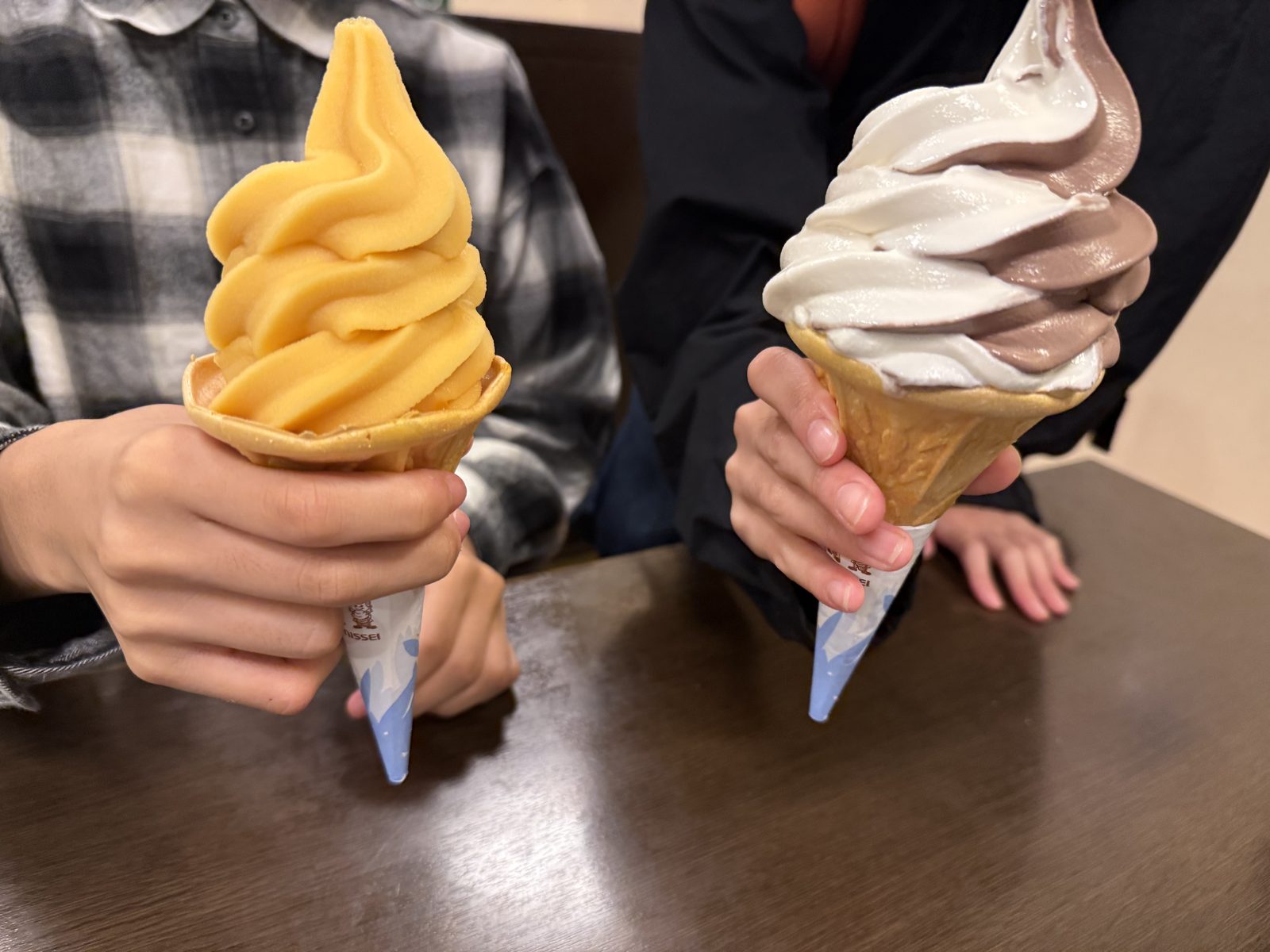 マンゴー味とチョコバニラミックスのソフトクリームを持つ子どもたちの手