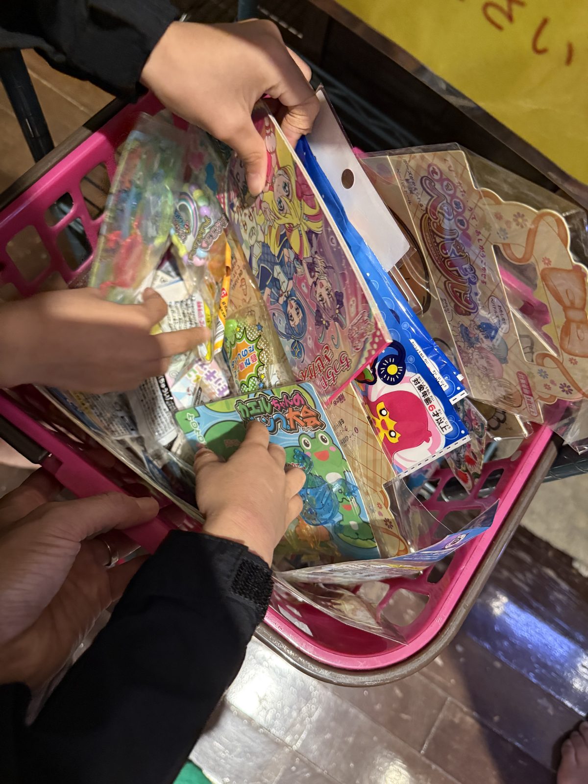 ピンクのカゴいっぱいに入ったお子様メニューのおもちゃを選ぶ子どもの手
