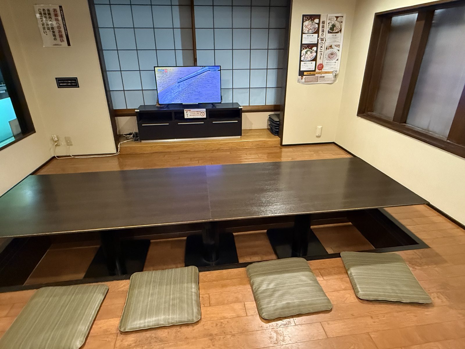 テレビの前にある掘りごたつの大きな座敷席。座布団が4枚並んでいる